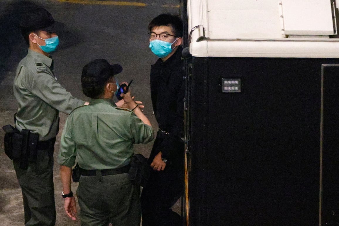 Two guards and a man in a dark blue suit, all wearing medical face masks