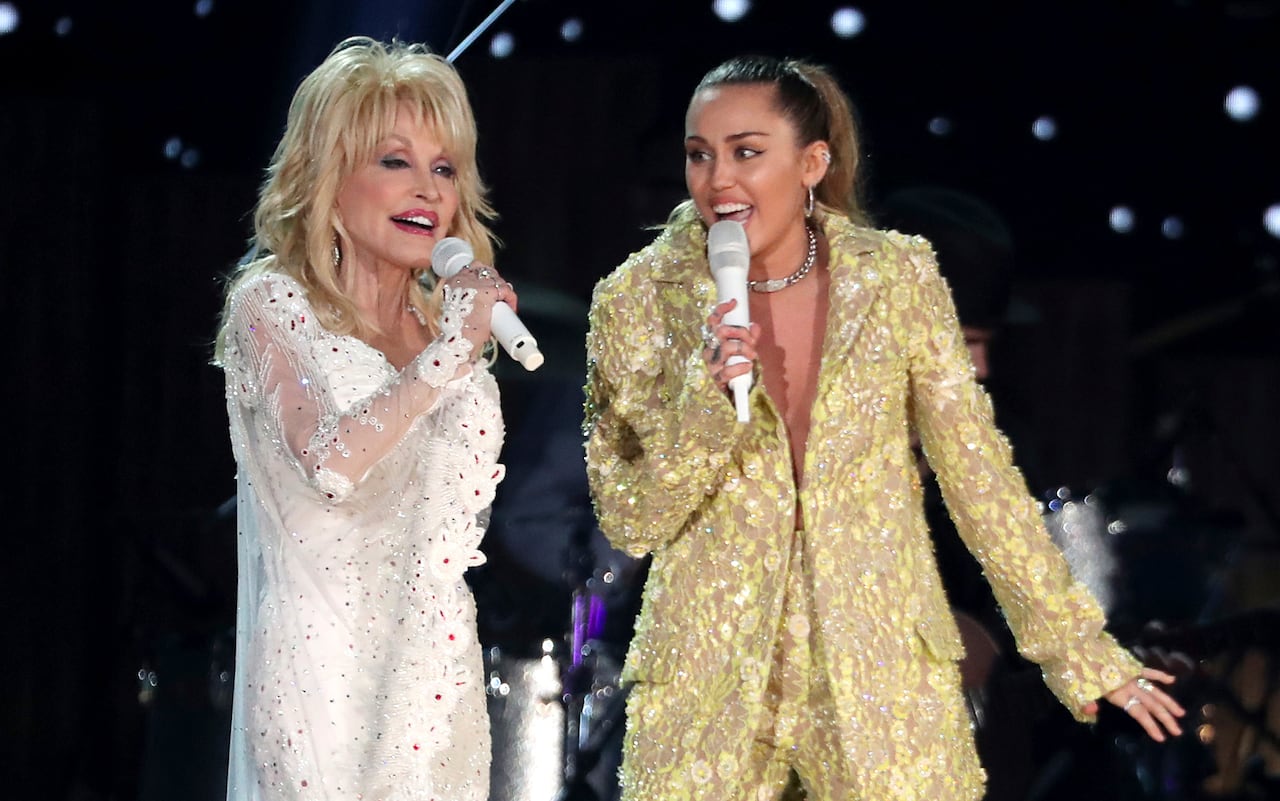 default-627 An older woman in a shiny white outfit sings onstage with a younger woman in a shiny gold outfit.