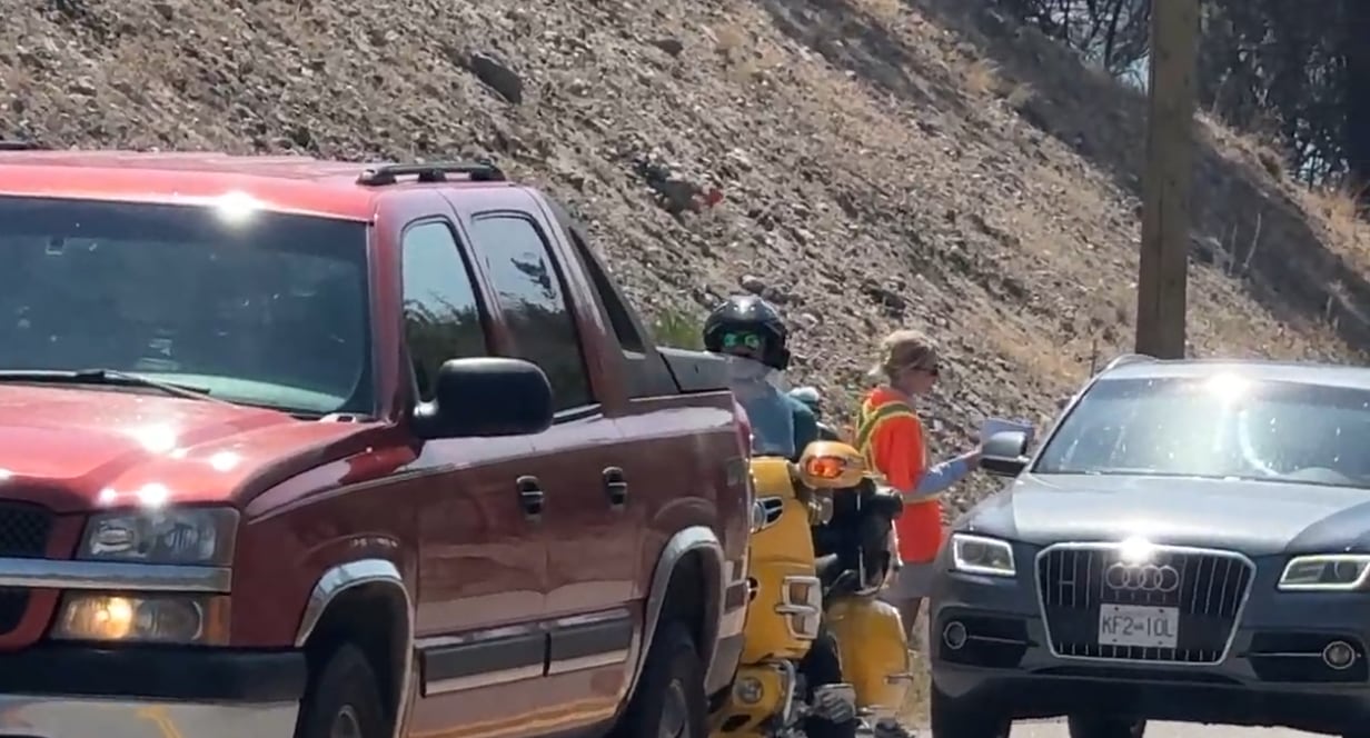 Person in high-visibility vest speaking to a driver in a car amidst a line of vehicles.