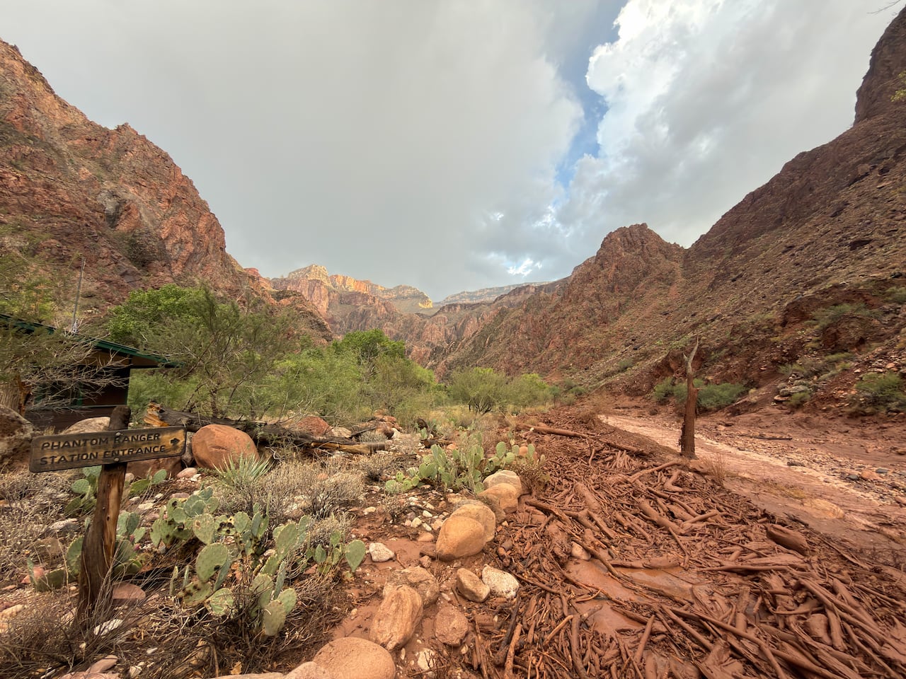 A muddy landscape with rocks and sticks is shown with mountains in the background. A wooden cross in the foreground is inscribed with the words 'Phantom Ranger Station Entrance.'